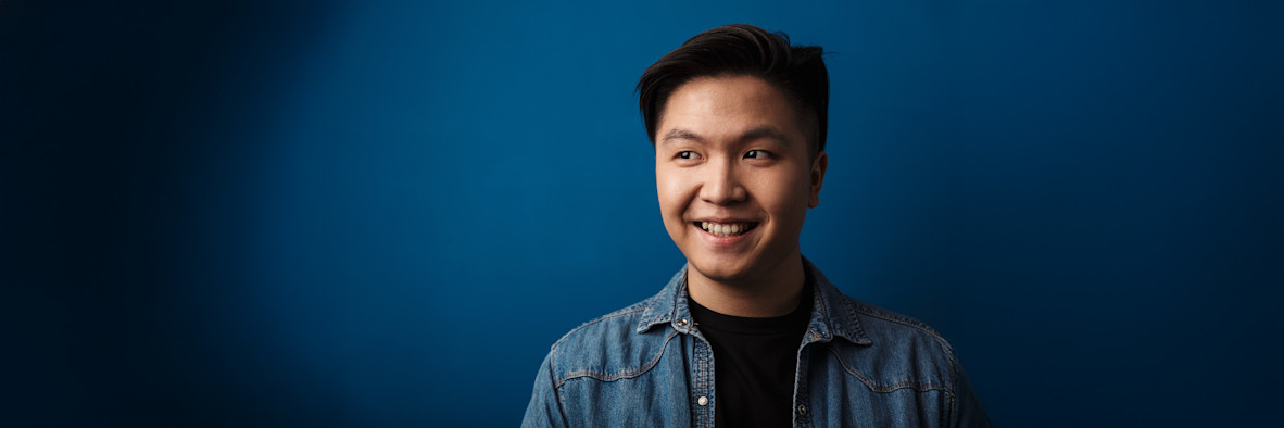 Ein lächelnder junger asiatischer Mann mit gesundem dunklem Haar vor blauem Hintergrund.