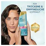Eine Frau hält eine Flasche Head & Shoulders DermaX Pro Shampoo, das die sanfte Pflege für trockene und empfindliche Kopfhaut mit Ceramid-Komplex bewirbt.