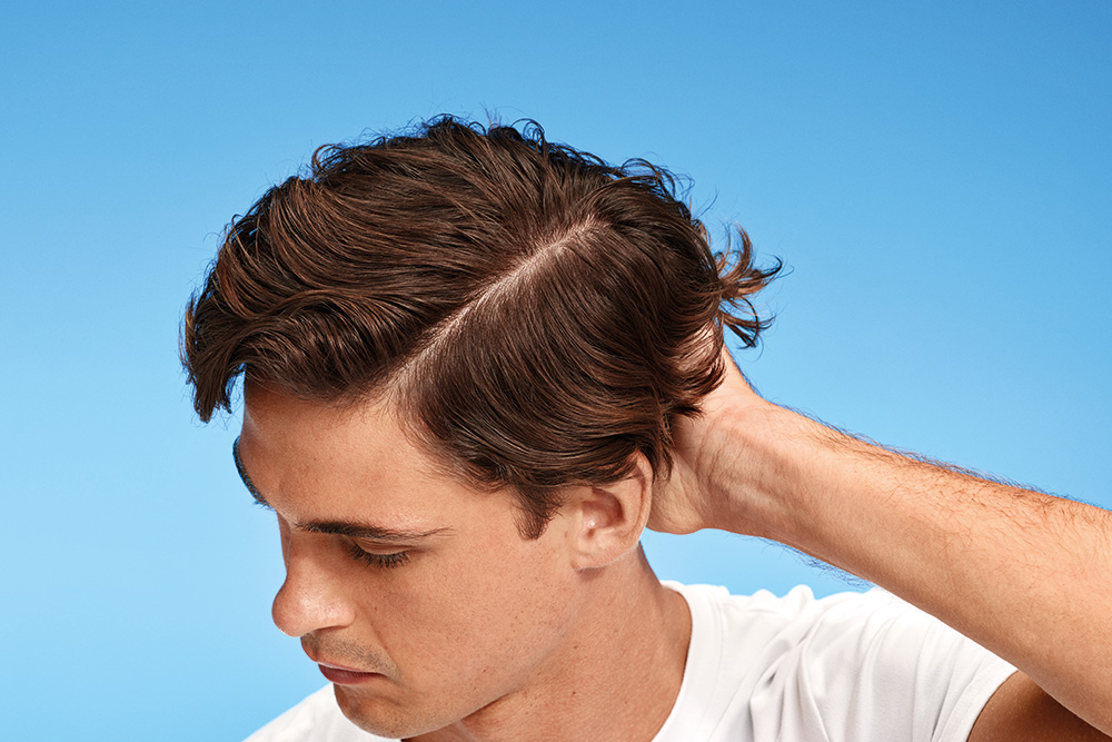 Nahaufnahme eines Mannes mit gescheiteltem braunem Haar, der seinen Nacken berührt.