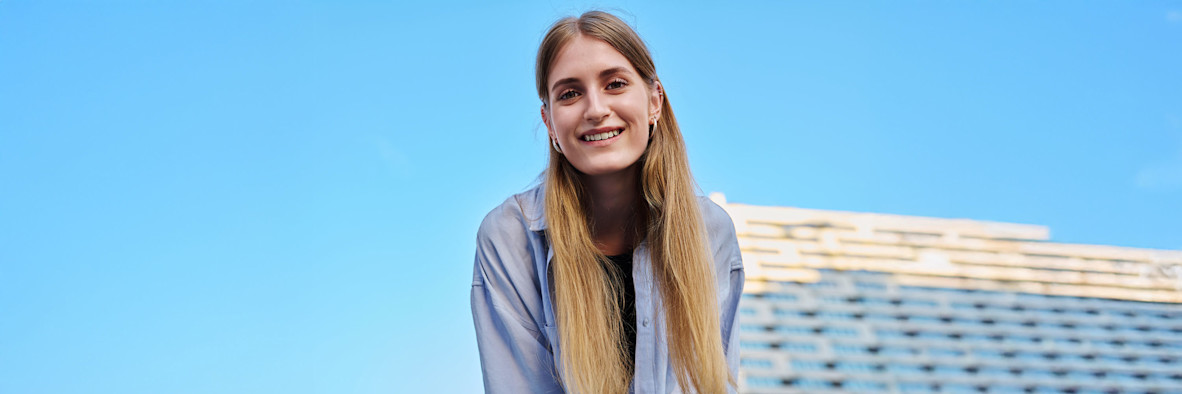 Eine lächelnde Frau mit langen, glatten Haaren, die im Freien vor einem blauen Himmel fotografiert wurde.