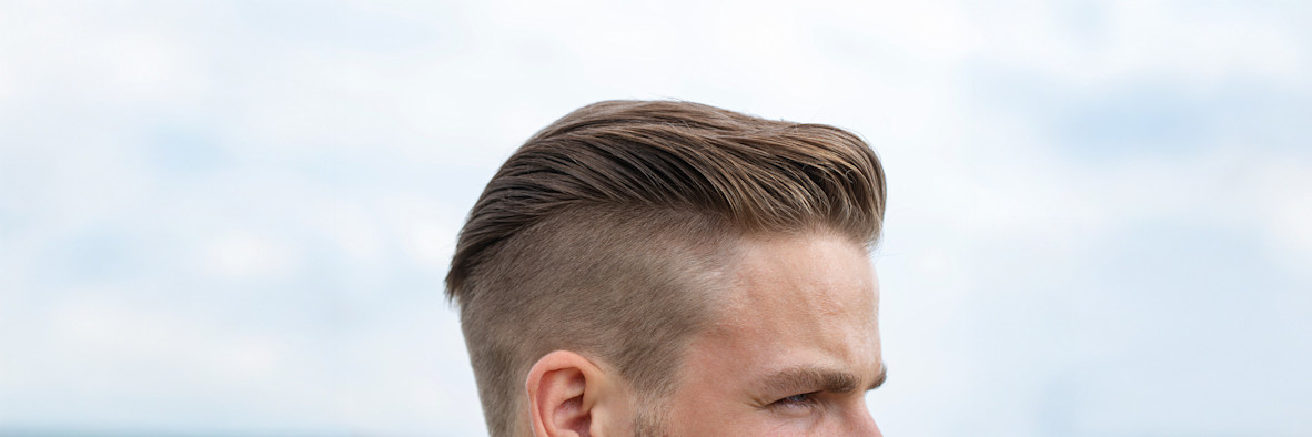 Seitenprofil eines Mannes mit einem scharf geschnittenen Undercut-Fade-Haarschnitt vor weißem Hintergrund.