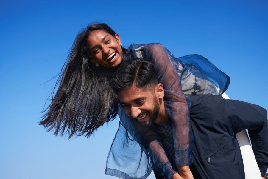 Eine Frau mit langen dunklen Haaren lächelt und umarmt einen lächelnden Mann