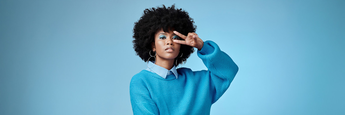 Eine Frau in einem blauen Oberteil zeigt nach oben, während sie ihr natürlich lockiges Haar berührt.