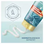 Shampoo-Flasche mit goldenem Deckel, aus der ein cremiges Produkt fließt; das Etikett hebt klinische Tests und den Koffeingehalt hervor.