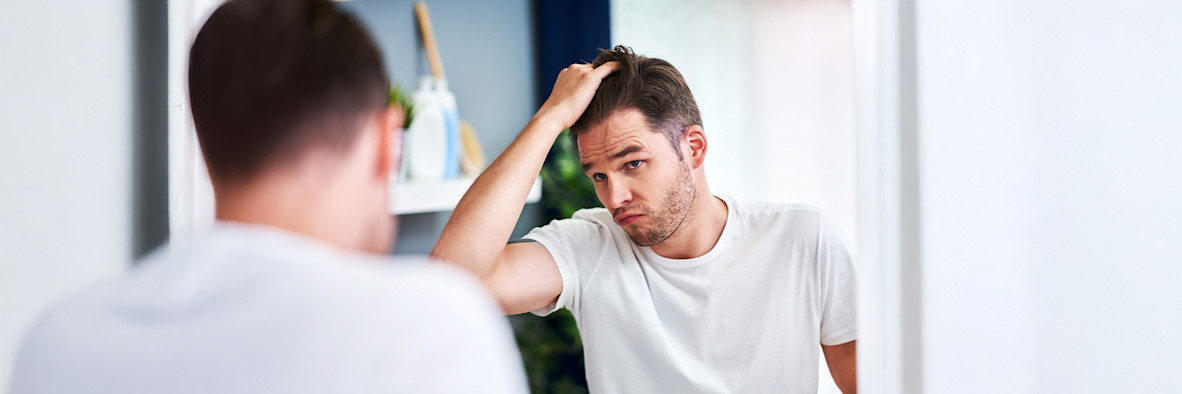 Ein Mann im weißen T-Shirt greift nach oben, um seine Kopfhaut zu berühren oder zu kratzen.