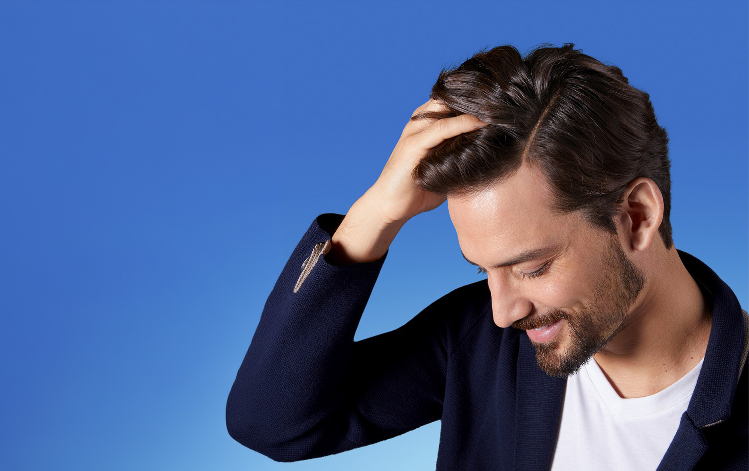 Der Mann mit dem glänzenden Haar lächelt und schaut zur Seite.