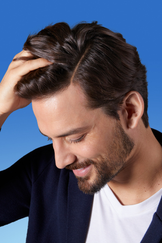 Mann mit gepflegtem Haar berührt seinen Kopf und lächelt.