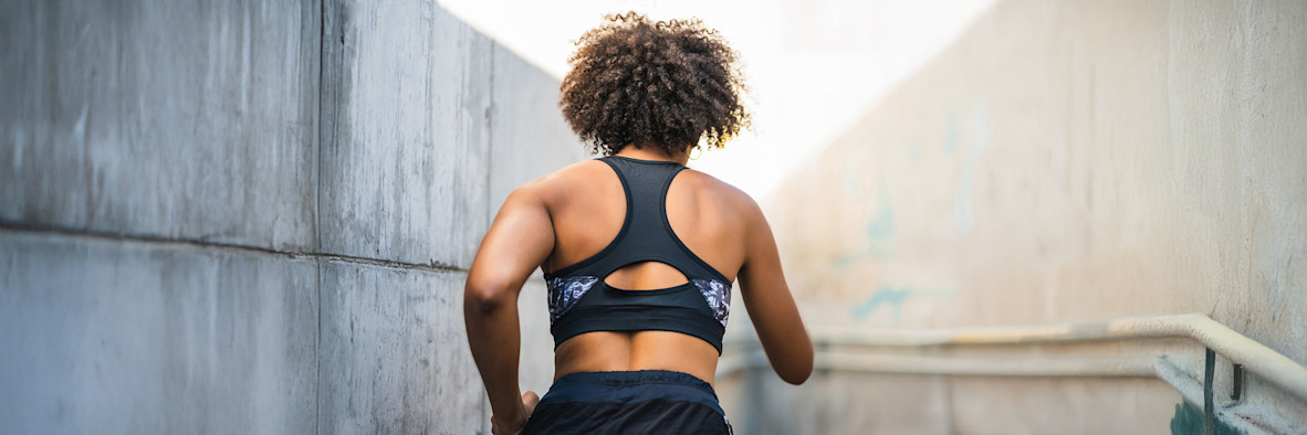 Eine Frau in einem Sport-BH mit natürlicher Afrofrisur posiert selbstbewusst.