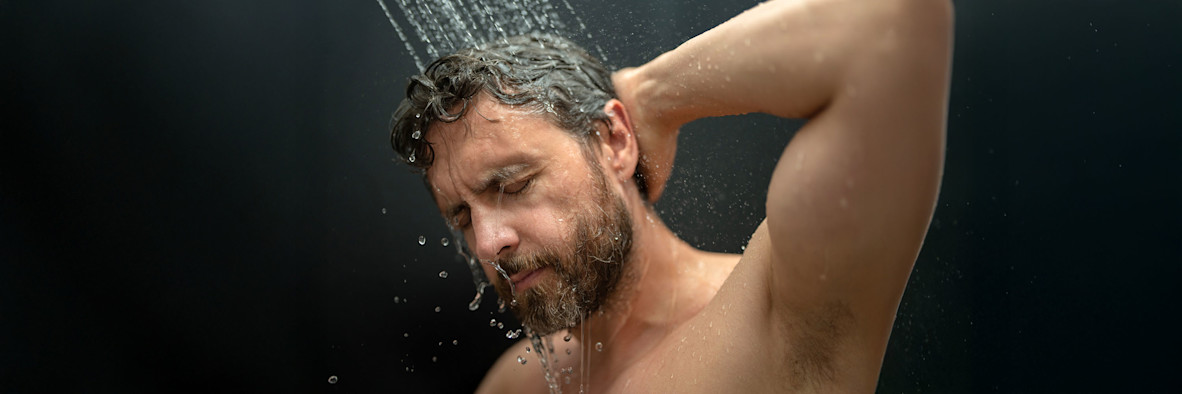 Ein bärtiger Mann schäumt Shampoo in seinem Haar unter der Dusche ein, die Augen geschlossen.