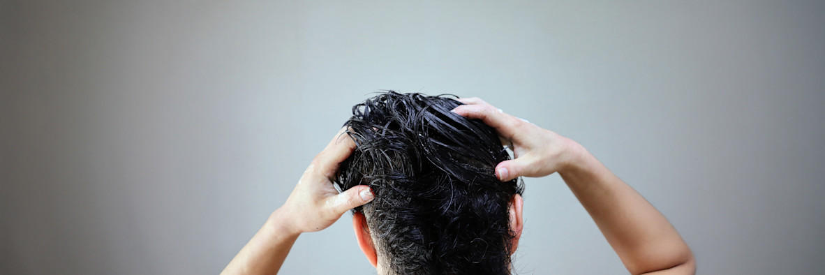 Eine Frau wäscht sich mit geschlossenen Augen die Haare, sichtbarer Schaum in ihren Händen.
