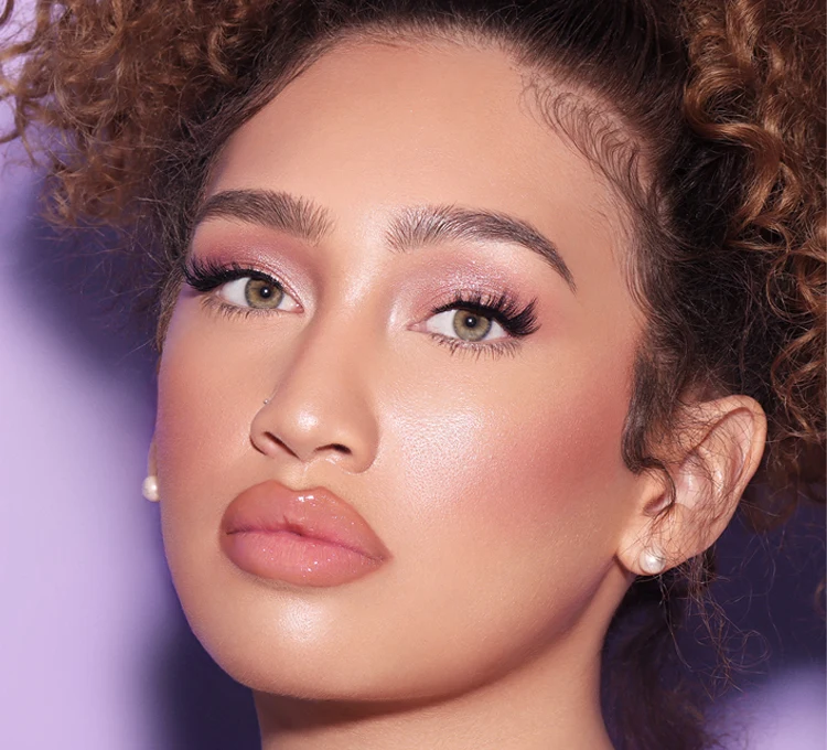 A woman with curly hair posing against a purple background wearing Lilly Lashes' Sensuous Half Lash.