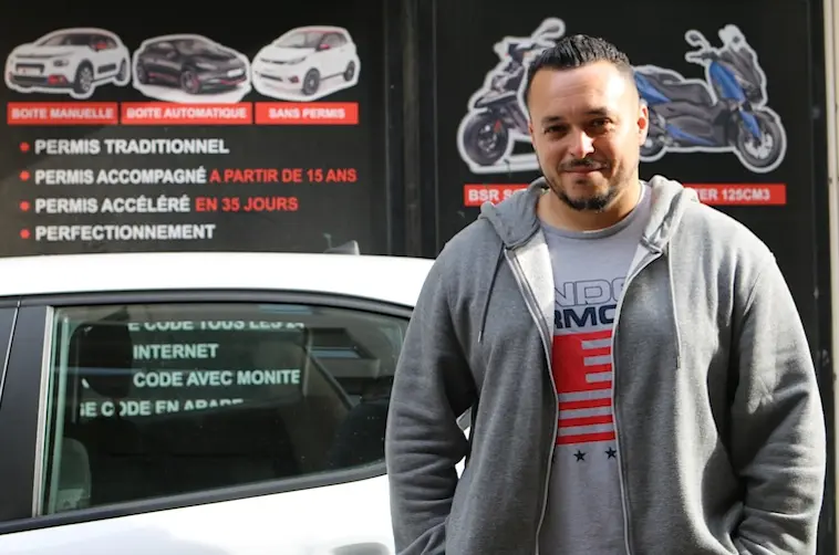 Enseignant de conduite par l'Adie debout devant son véhicule de fonction et son auto-école
