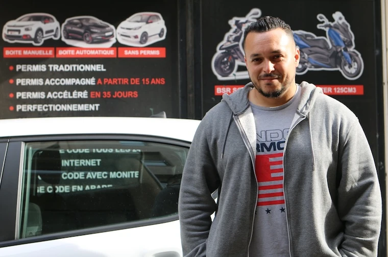 Enseignant de conduite par l'Adie debout devant son véhicule de fonction et son auto-école