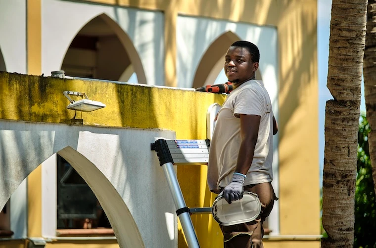 Entrepreneur financé par l'Adie contre un mur d'un bâtiment debout sur son échelle