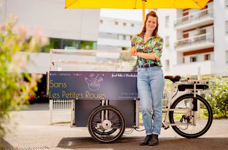 Entrepreneuse financée par l'Adie appuyée sur son stand professionnel à vélo