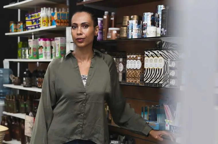 Entrepreneuse SARL financée par l'Adie debout devant ses étagères de produits