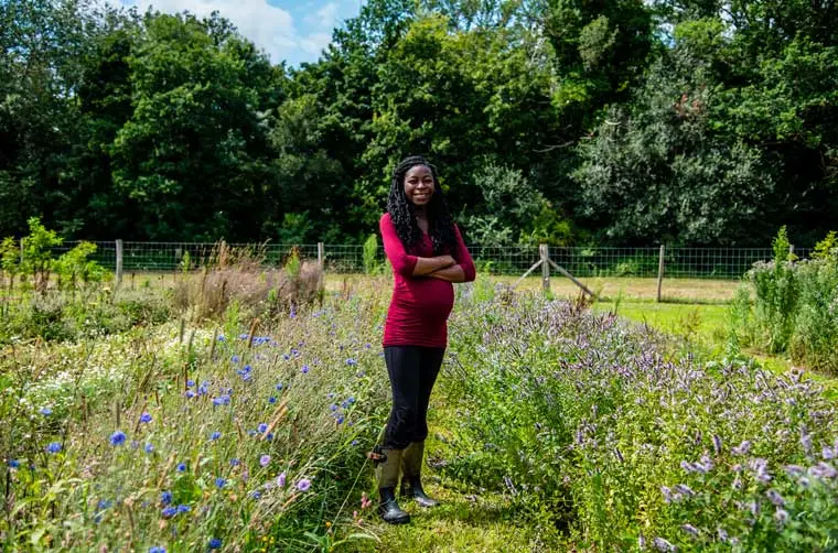 Entrepreneuse financée par l'Adie enceinte, debout dans son champ de fleurs