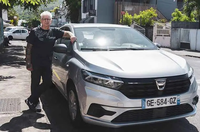 Professionnel financé par l'Adie se tenant appuyé sur sa voiture blanche 