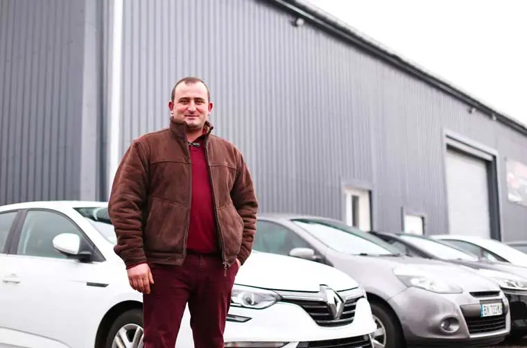 Entrepreneur financé par l'Adie devant son garage et ses voitures d'achat-revente