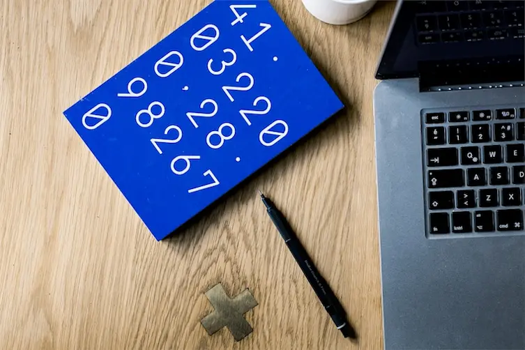 Carnet de calculs posé sur une table à côté d'un ordinateur portable