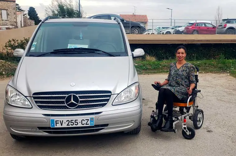 Soumiya, assistante administrative financée par l'Adie, assise dans son fauteuil à côté de son véhicule professionnel