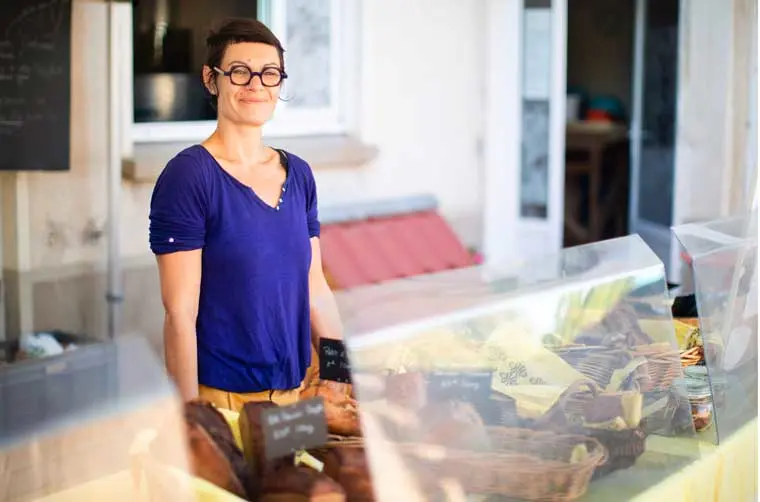 Entrepreneuse financée par l'Adie souriant derrière son comptoir