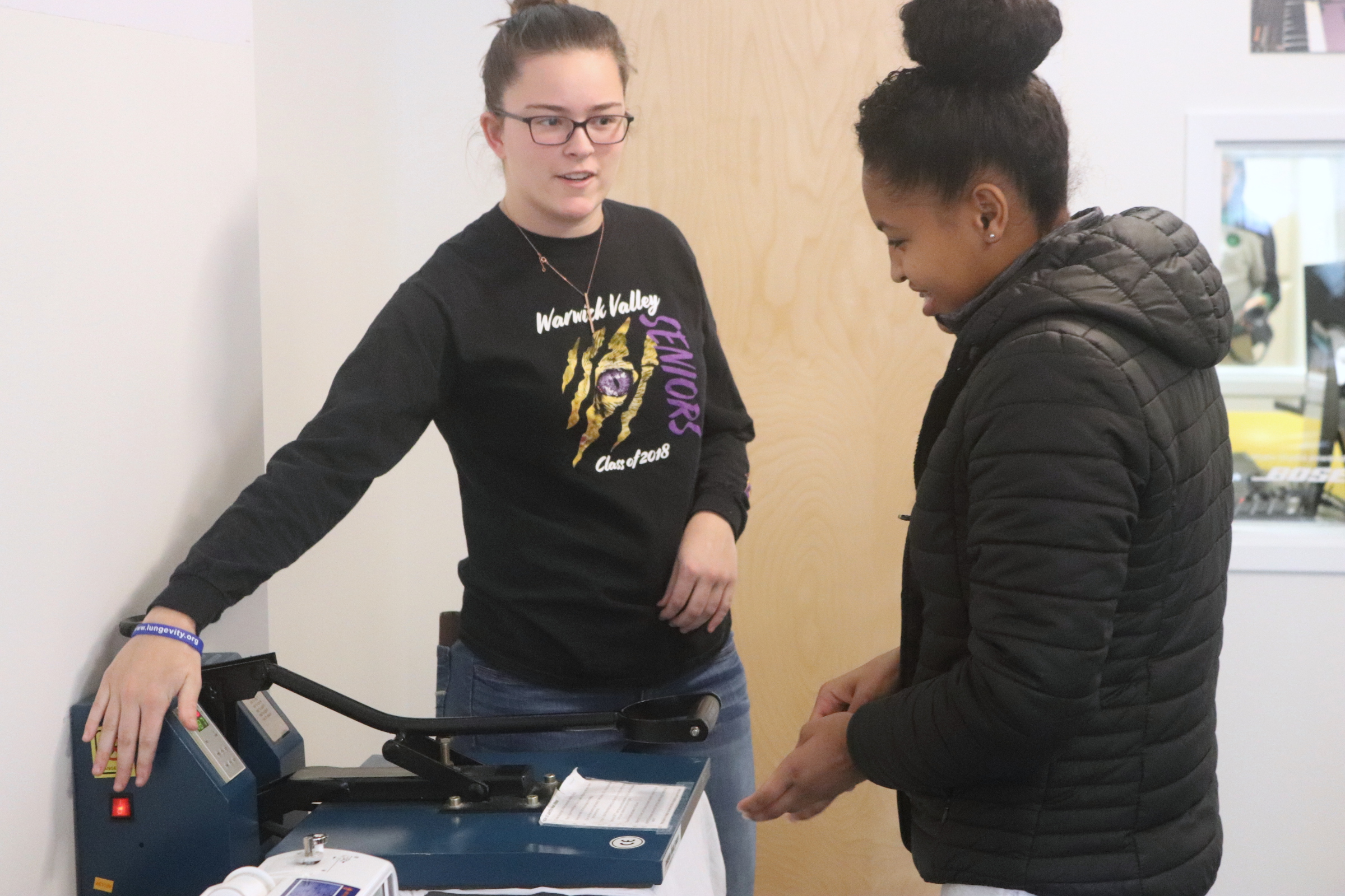 A mentor from Northeastern university (left) helps a teen girl use a heat press to make a custom t-shirt. (Source: Clubhouse Network)