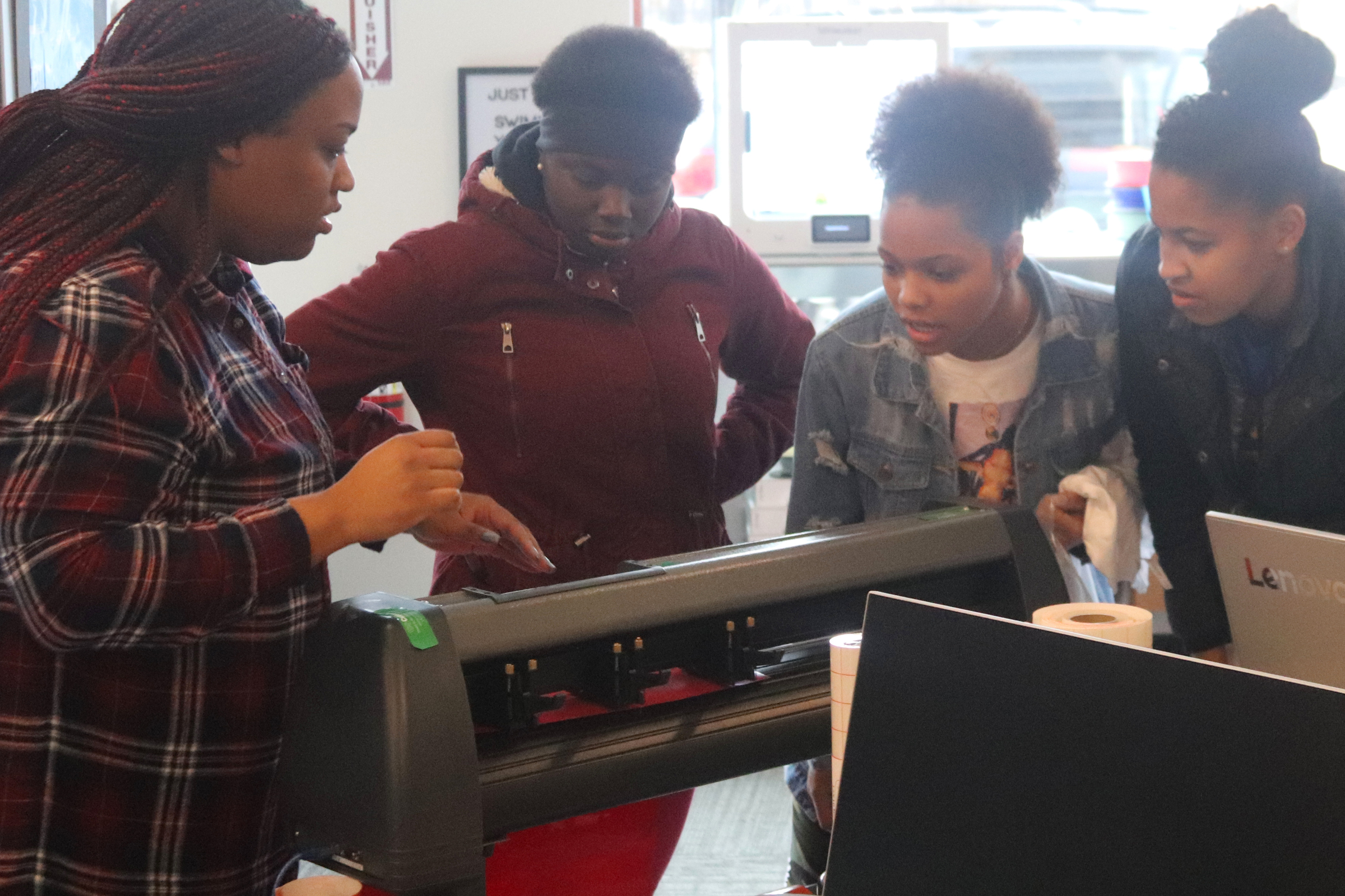 Flagship Clubhouse staff member and mentor Dominique Williams (left) helps a group of teen girls use a vinyl cutter. (Source: Clubhouse Network)