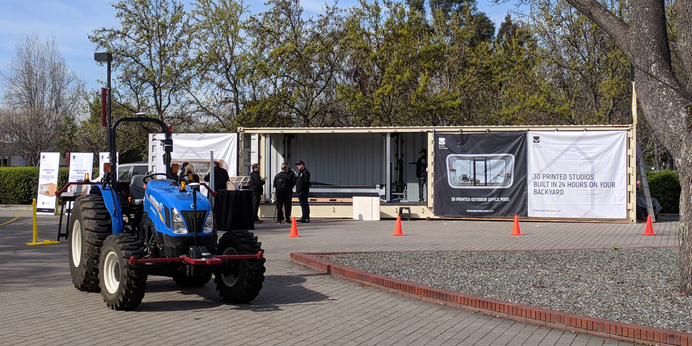 Outside, an autonomous tractor goes in circles next to a 3D printer making a portable office. Photo Credit: Tony Wan