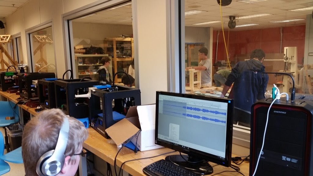 A giant window divides the AHS workshop, with some students working on computers while others use laser cutters.