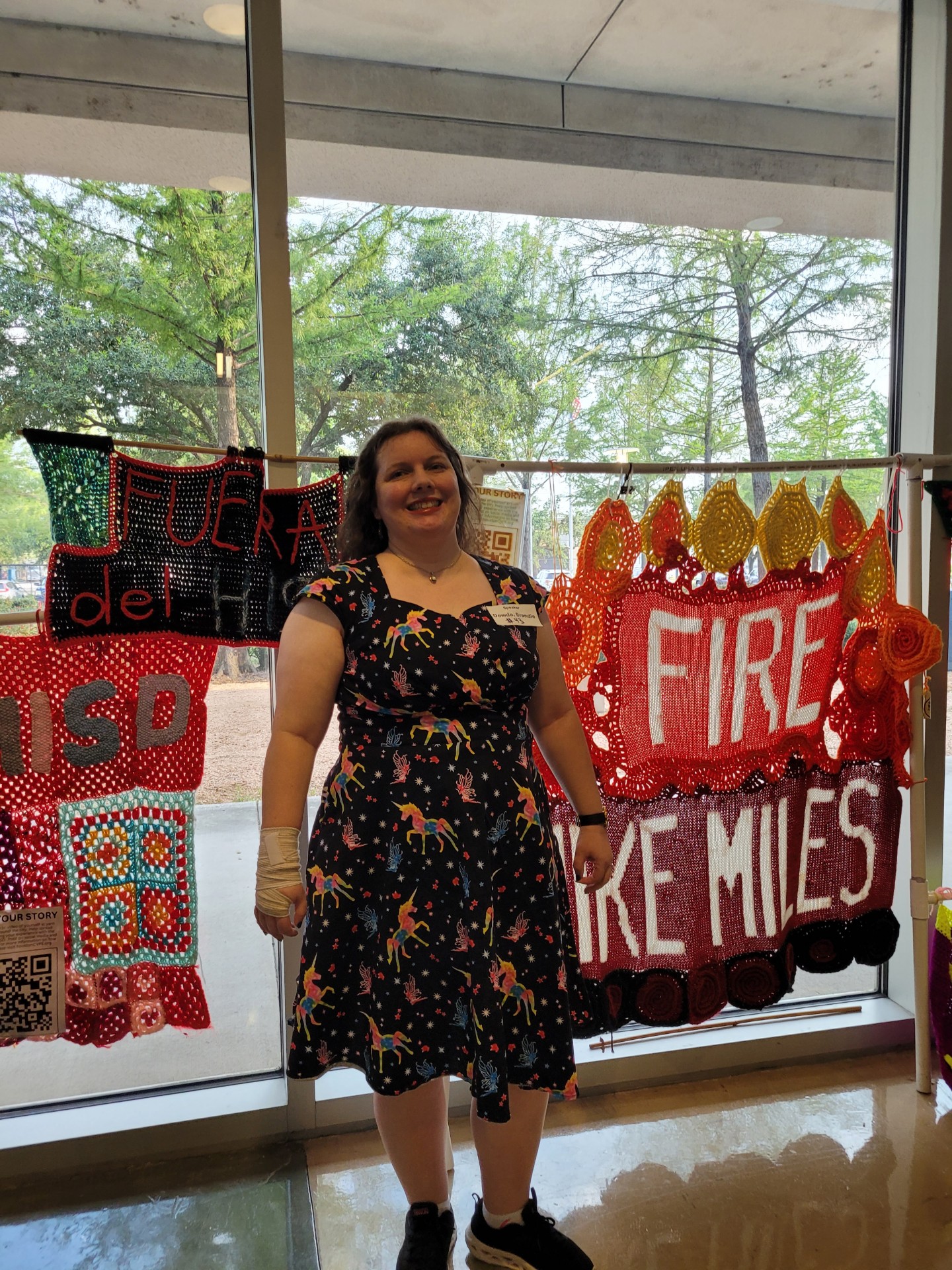 Librarian Brandie Dowda poses in front of knitted protest signs before speaking at a board of managers meeting in August 2024. Photo courtesy of Dowda.