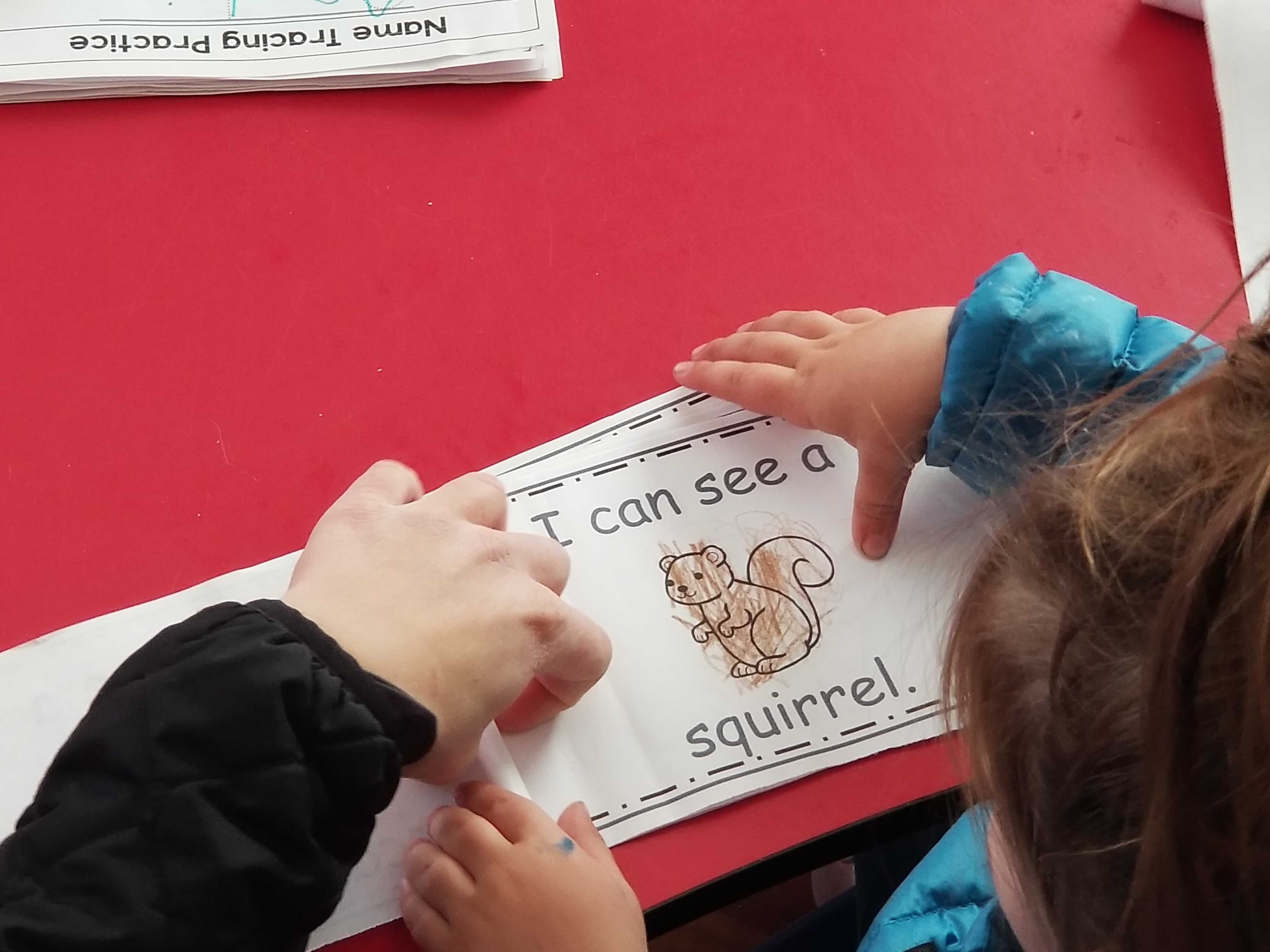 Teacher Sam Morrison helps Sophia, a girl enrolled at Whitesides’ home-based preschool in Nevada, read from a book she colored. Credit: Wade Tyler Millward / EdSurge