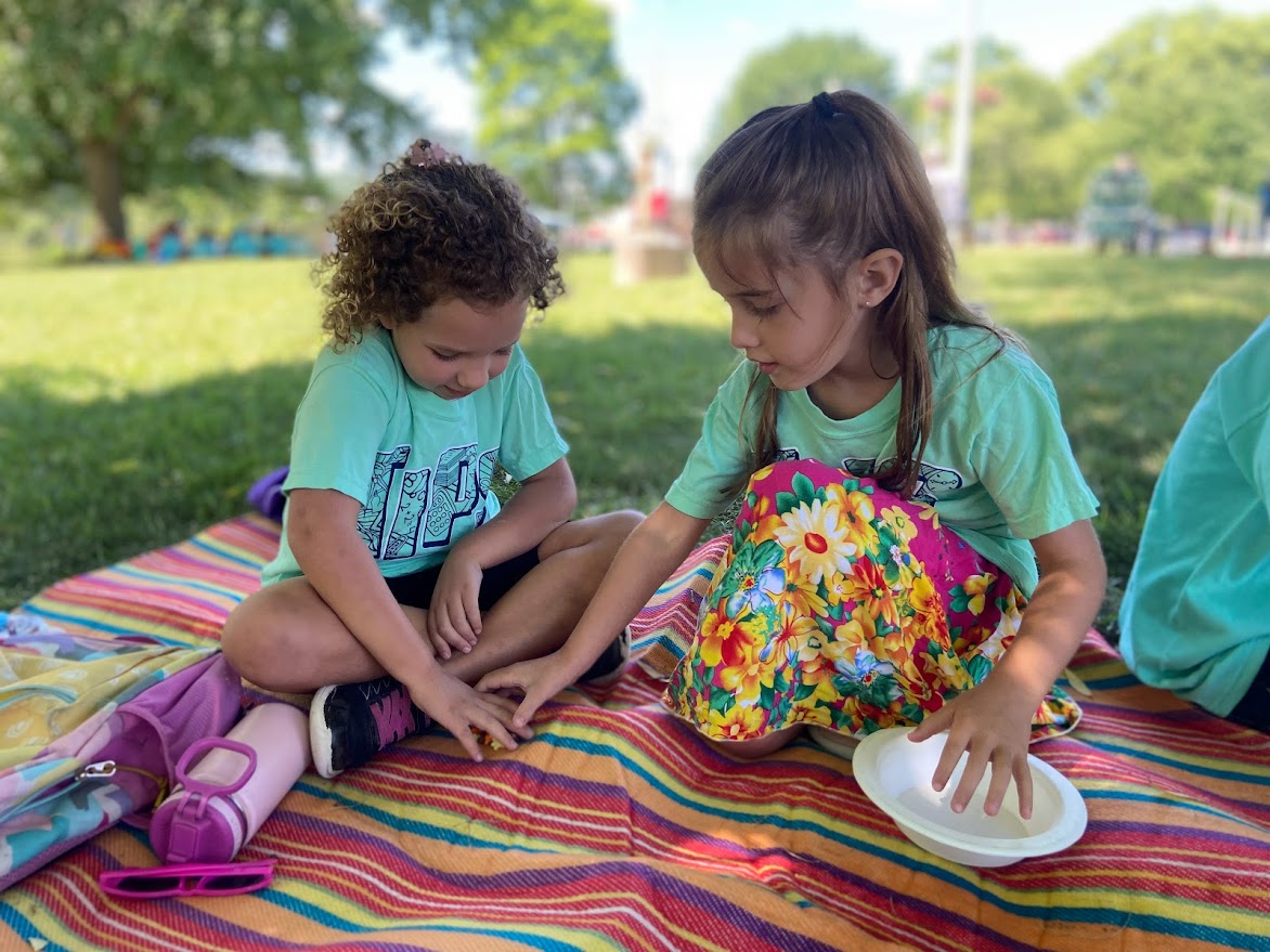Elementary school-aged children play on a blanket under a tree during Teachers in the Park summer learning. (Courtesy of Matt Hathaway)