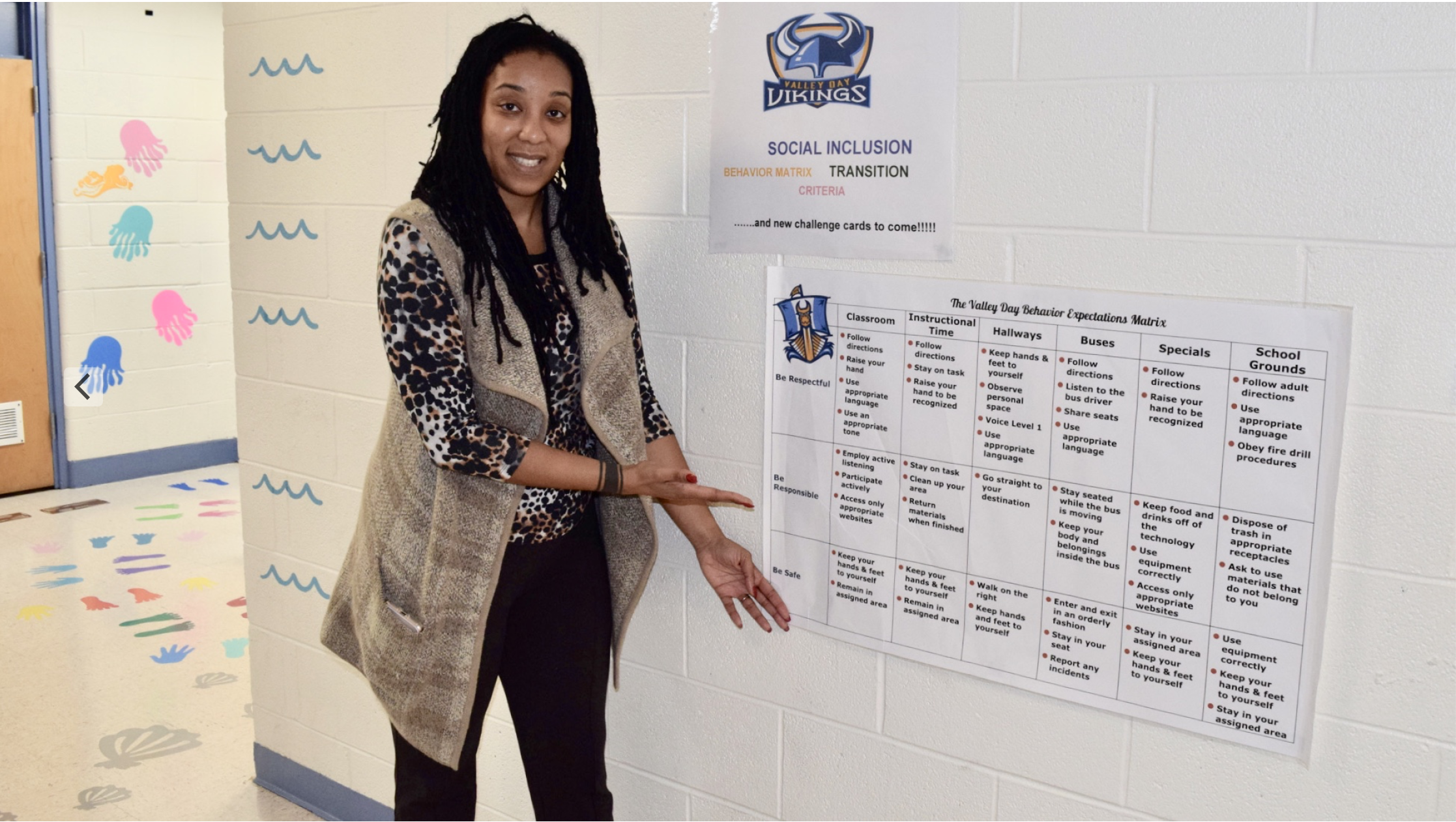 Jessica Milton, the principal and education director at Valley Day, highlights the school's behavior expectations matrix in the main hallway of the building. (Emily Tate / EdSurge)