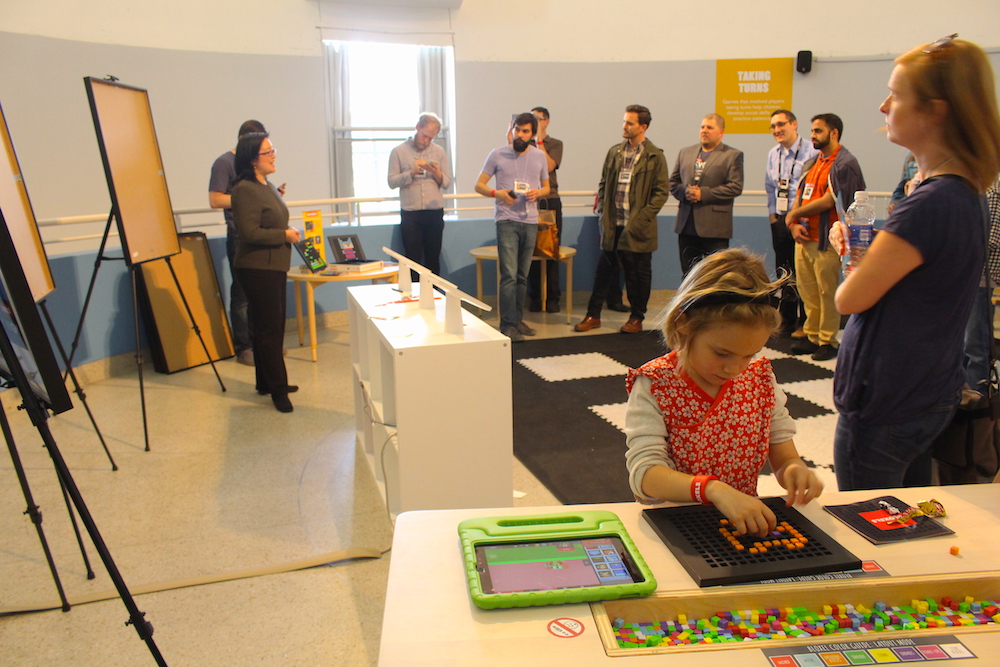 Photo by Tom Durkin. A child plays with a Bloxels board while Carol Tang, the museum's executive director, addresses the crowd.