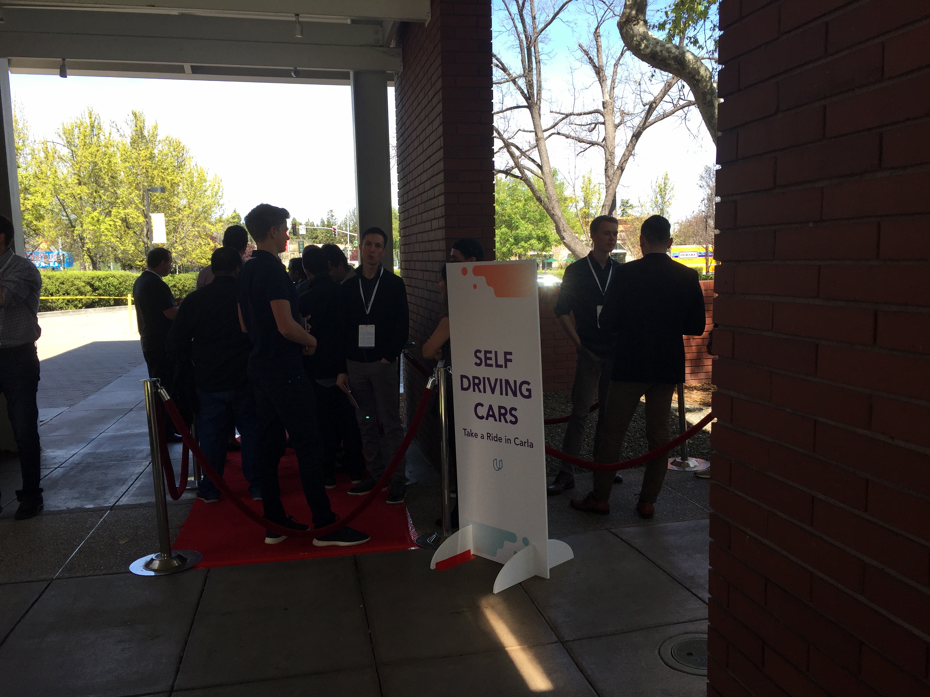 Conference attendees wait in line on a red carpet to ride in Udacity's self-driving car.
