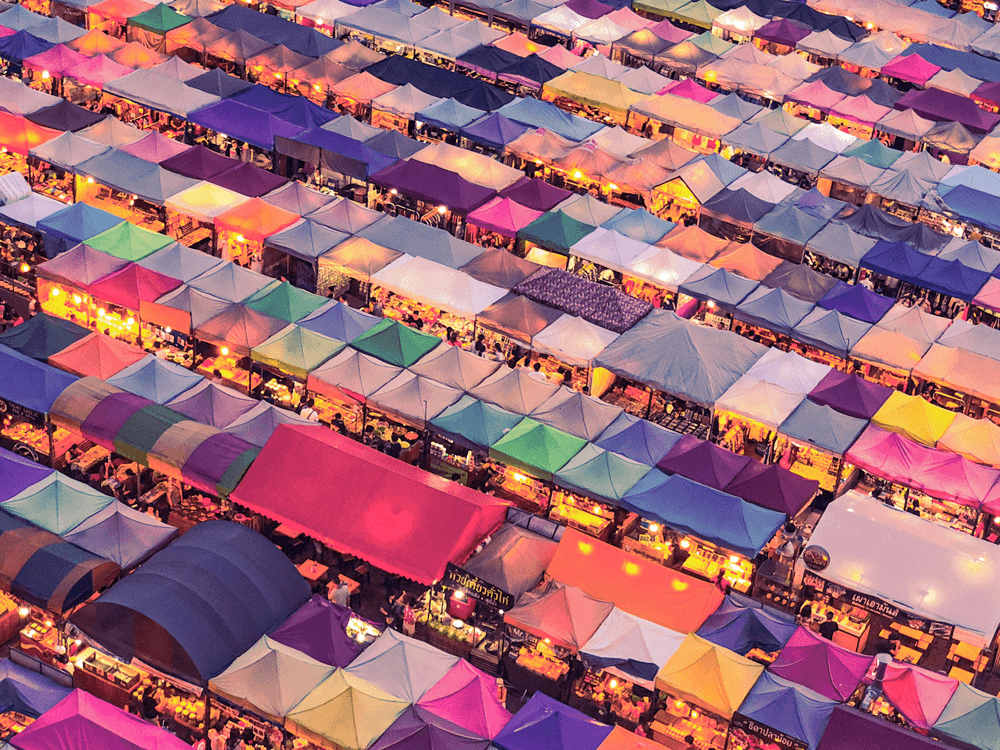 Multi-coloured rows of market tents seen from above.