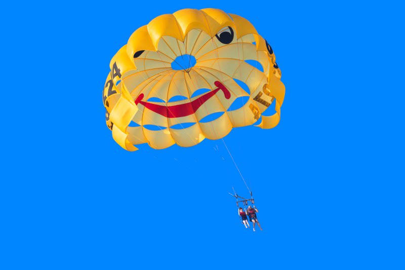 Two people are suspended from a parachute with a big smiley face on it.