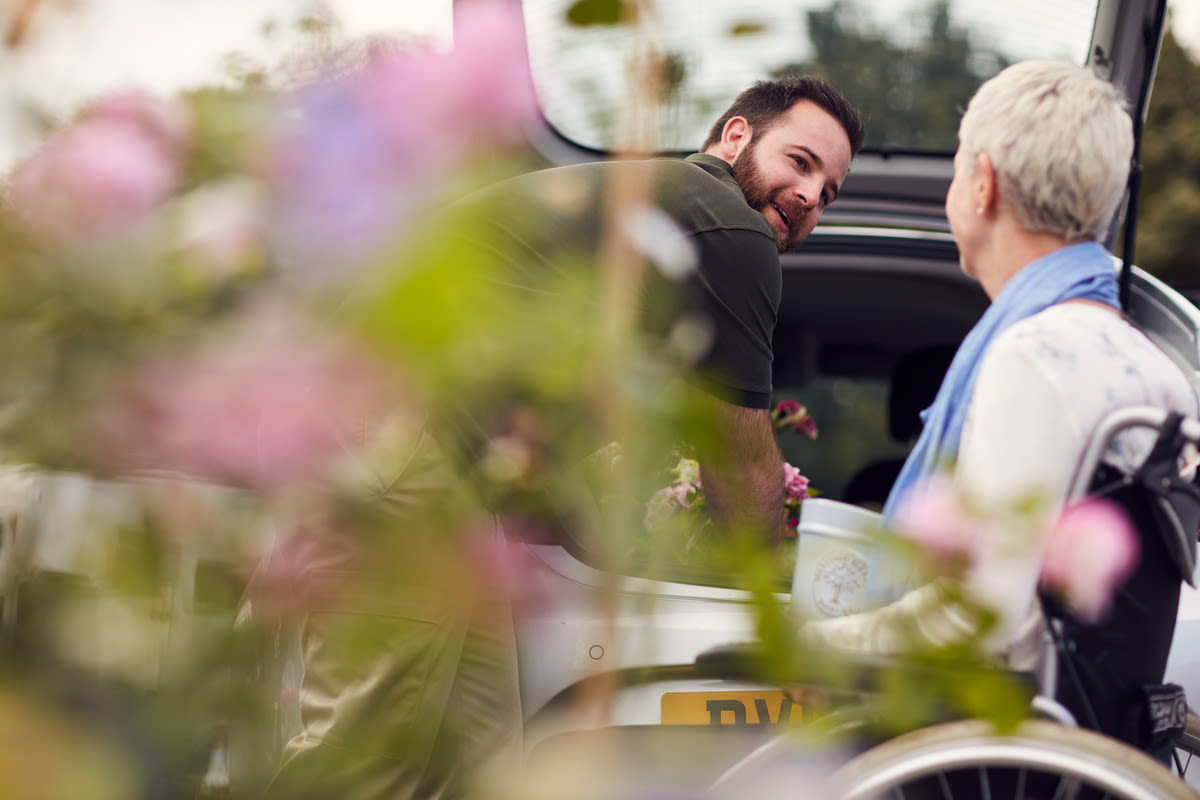 A man helping a woman in a wheelchair pack things in the boot
