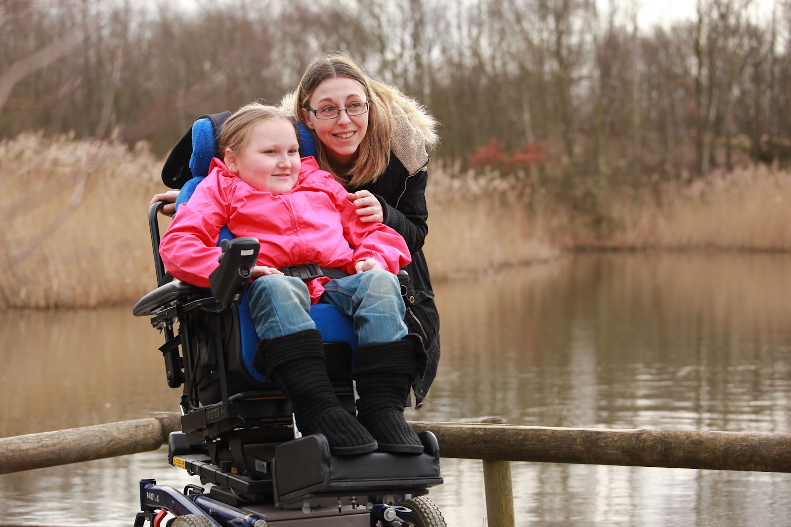 A woman crouching by a little girl in a powered wheelchair