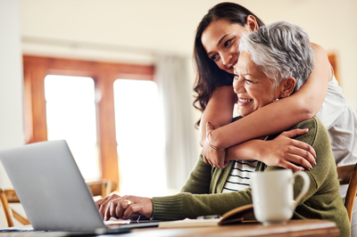 A young woman helping her family member on a laptop, smiling
