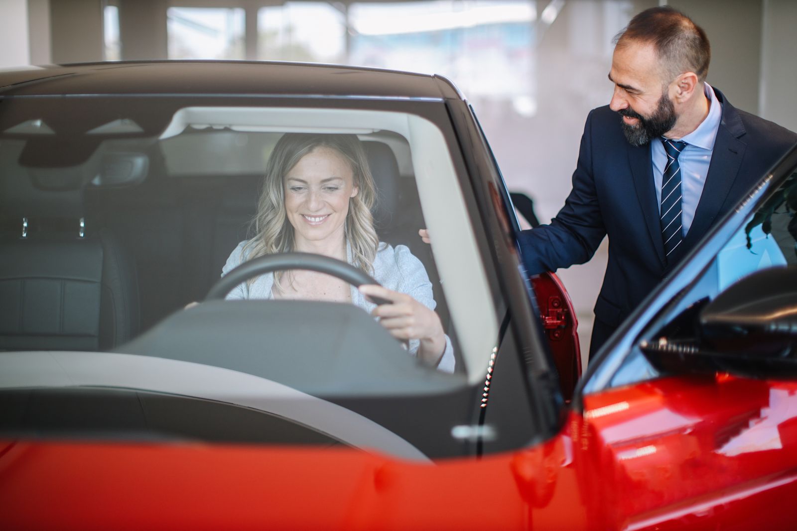 Woman sitting in a new car with a man outside talking to her