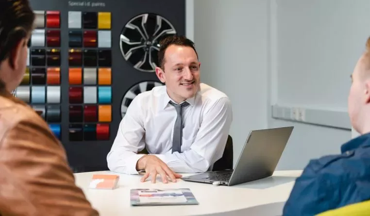 A dealer talking to two people in a dealer showroom