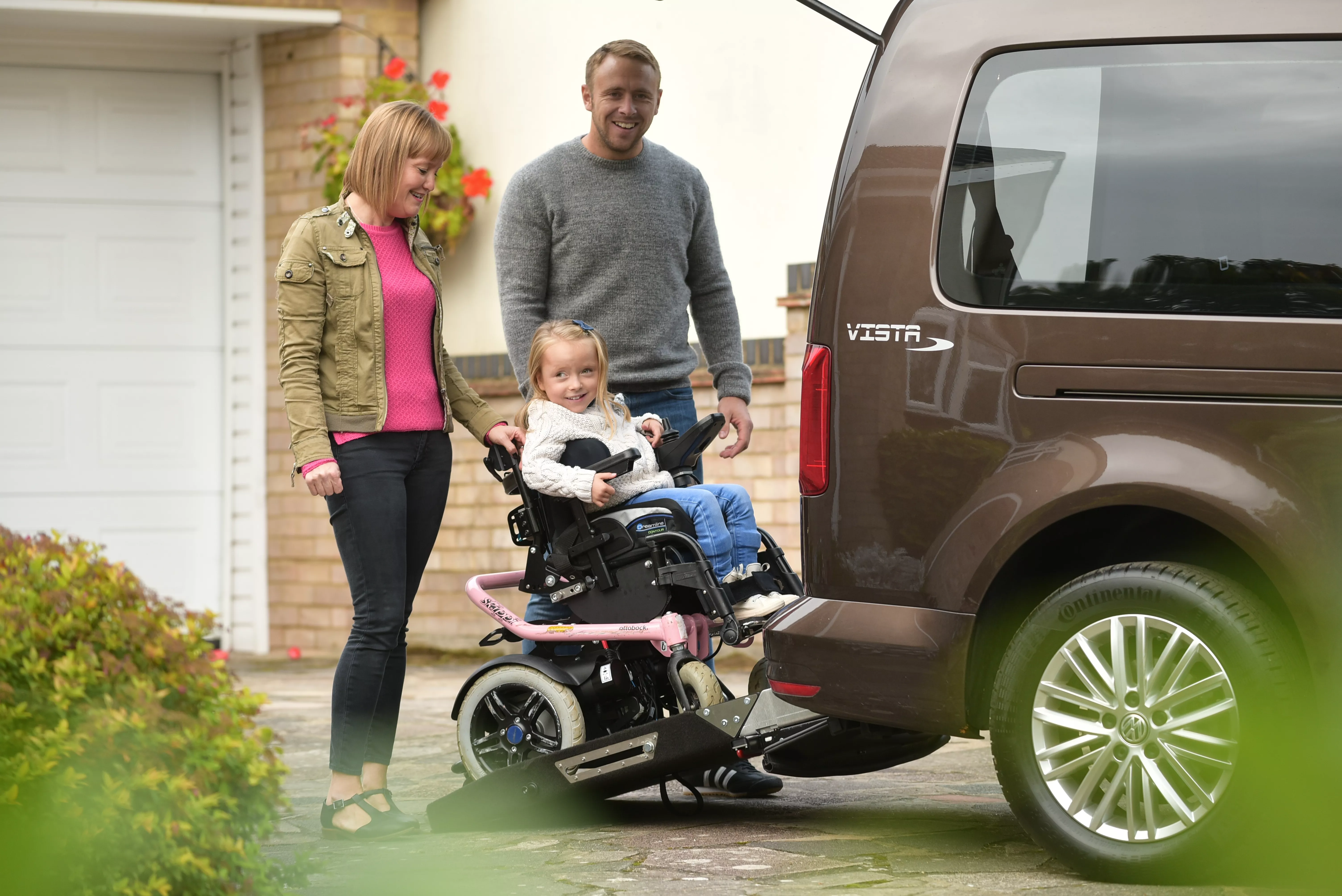 A family helping a little girl in a wheelchair use a rear ramp on a WAV