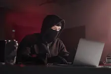 Ein Mann im Hoodie und Maske sitzt am Laptop und beschäftigt sich mit Internet-Selbstjustiz.