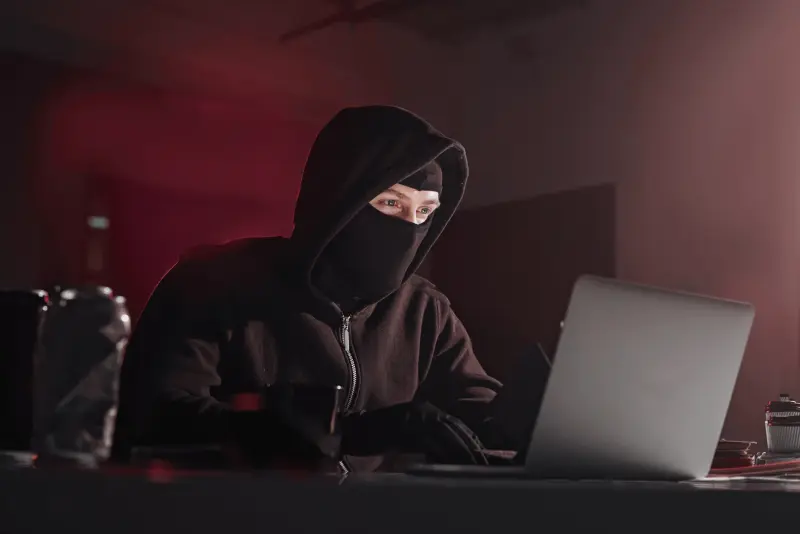 Ein Mann im Hoodie und Maske sitzt am Laptop und beschäftigt sich mit Internet-Selbstjustiz.