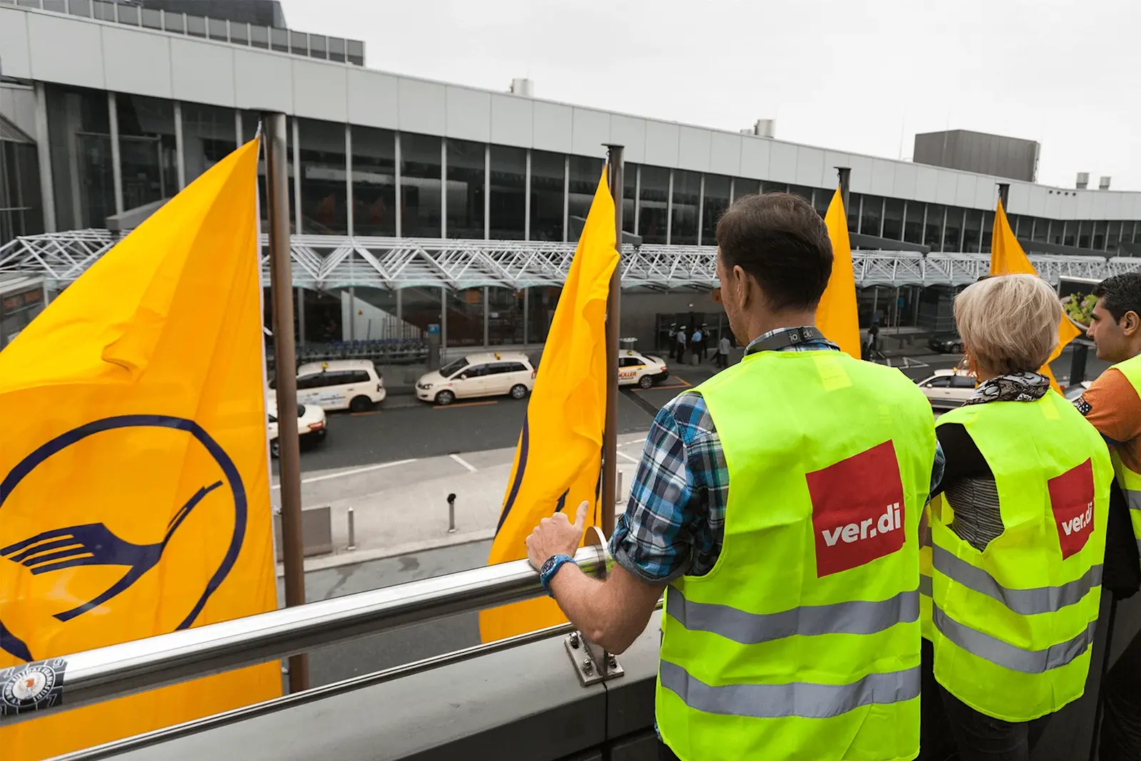 Drei Personen in gelben Westen stehen auf einer Brücke während des Streiks am Flughafen. 