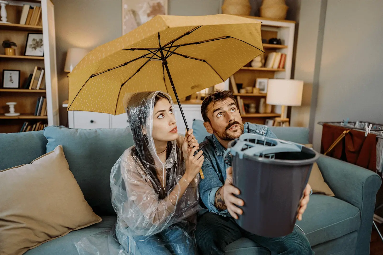 Ein Mann und eine Frau sitzen auf einer Couch und halten einen Regenschirm, um sich vor Wasserschaden zu schützen.