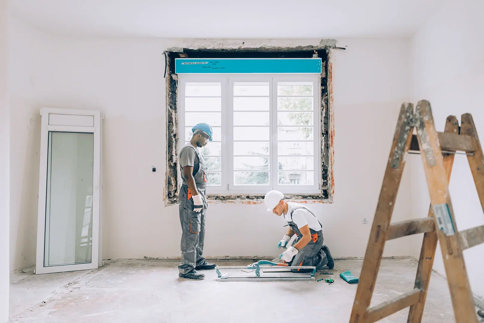 Foto: Zwei Handwerker setzen in einer Wohnung ein neues Fenster ein.