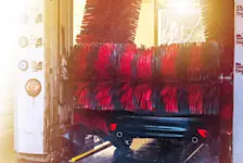Foto: ein dunkles Auto steht in der Waschanlage und wird eingeschäumt.